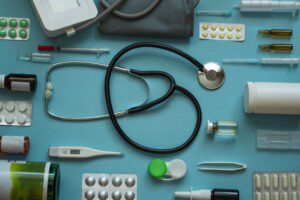 Top view medical flat layout: stethoscope, thermometer, syringe, pills, spray, lenses on blue background - top view flat mockup