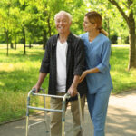 Happy nurse assisting elderly man with walking frame at park