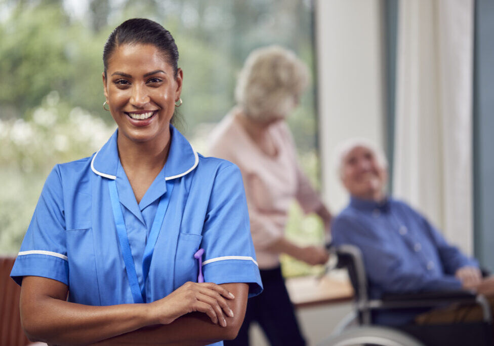 Portrait Of Female Nurse Or Care Worker Making Home Visit To Senior Couple With Man In Wheelchair